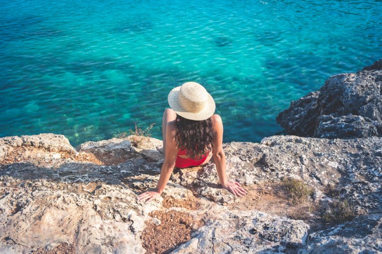 woman in hat and red bikini sitting on rock near water